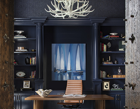 Custom home study with darck blue floor to ceiling shelves and cabinets. Deer antler chandelier with a medium brown wood desk and Eams style leather chair.